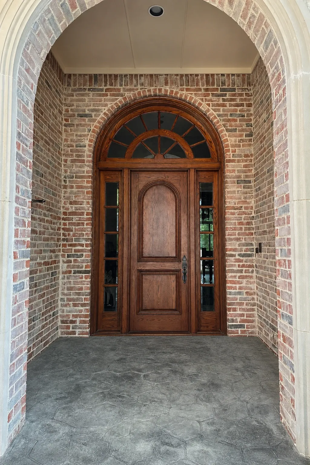 Original wooden entry with divided sidelights and a fanlight inside a brick arch