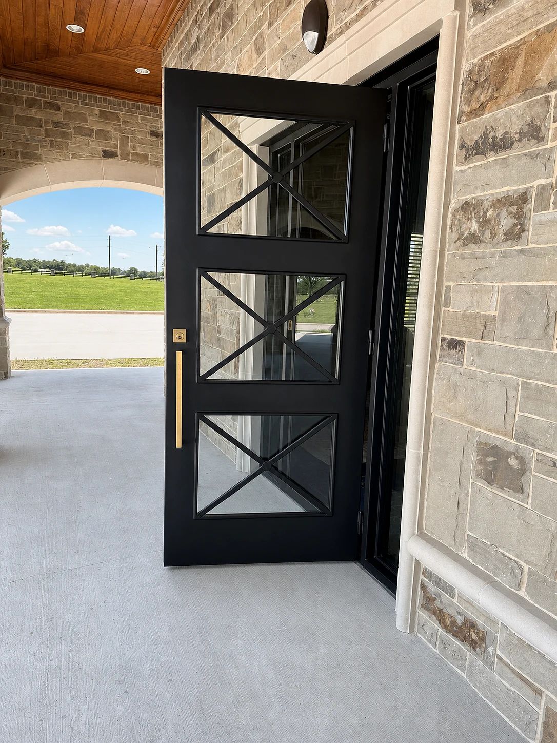 Open dark-bronze X-divided steel entry against the stone facade at Ridgeview West Memorial Park in Frisco