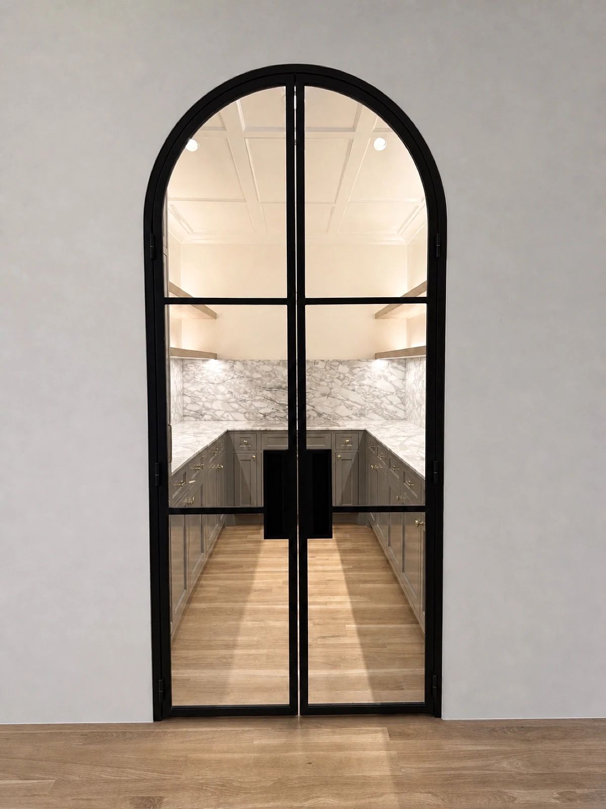 Full-arch black steel-and-glass pantry double door viewed from the kitchen