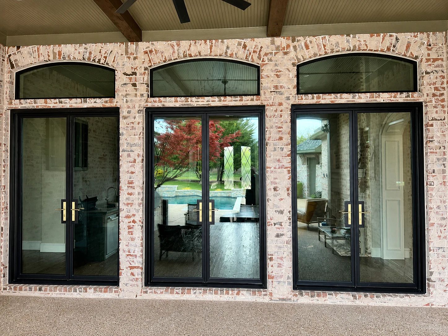 Exterior elevation of three black steel patio double doors with matching shallow arched transoms in Lucas, Texas