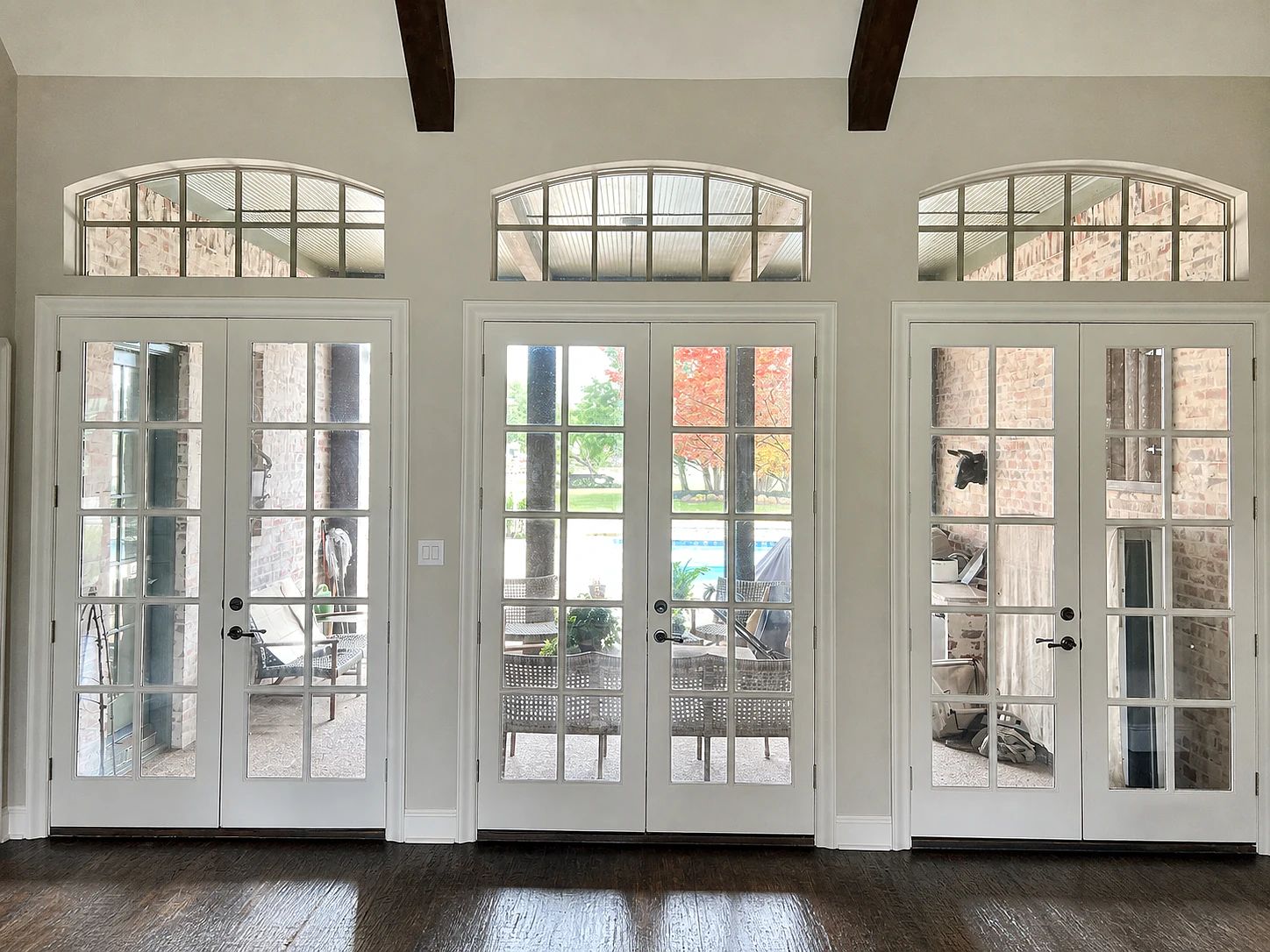 Lucas patio wall before replacement with three white French-door pairs and divided arched transoms
