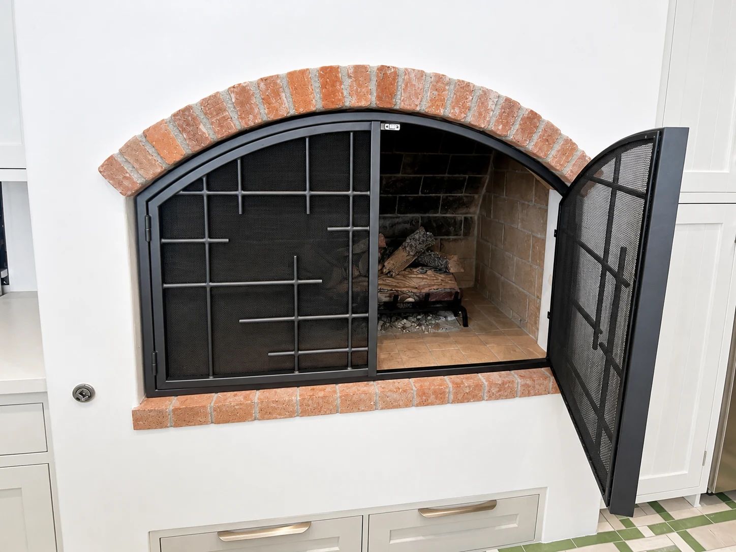 One hinged panel of a custom arched fireplace screen opened to show firebox access