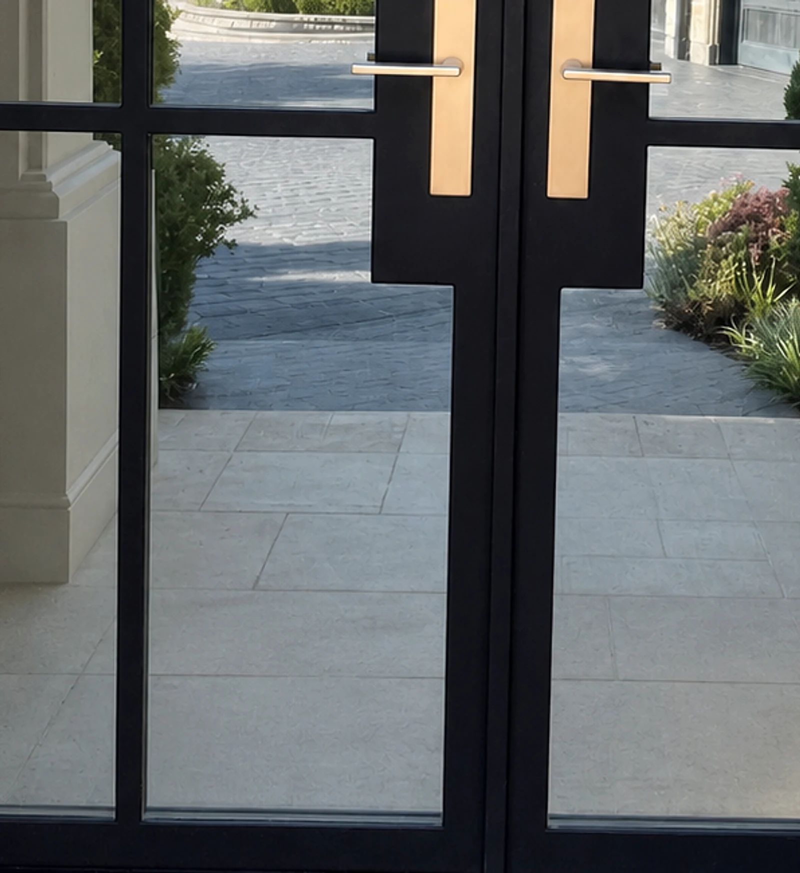 Close view of the arched black steel smart-glass entry’s center lock housing and satin-brass hardware