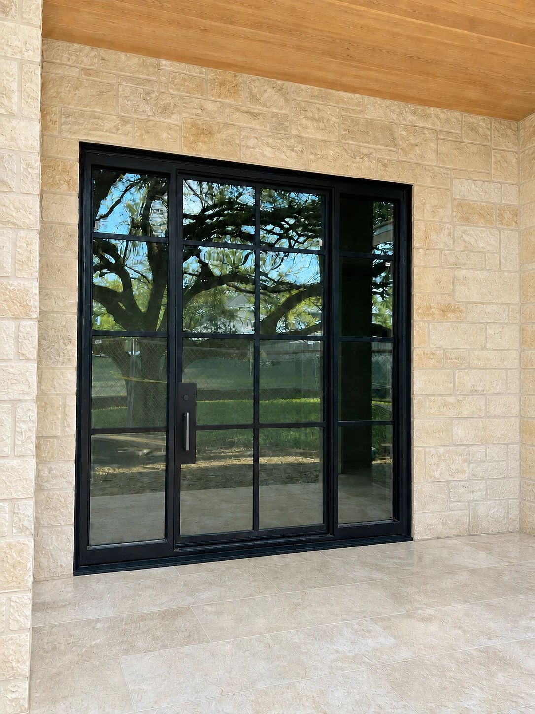 Black steel entry assembly with a modern black pull, central operable door, and fixed glazed panels in a limestone Preston Hollow residence