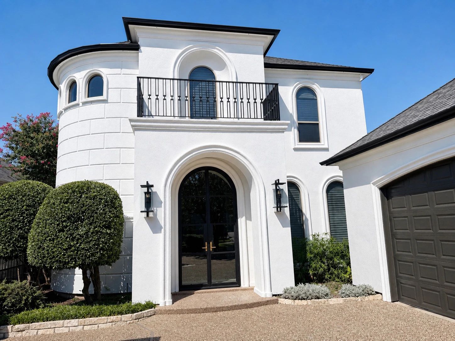The arched iron entry and balcony railing seen in daylight from the drive
