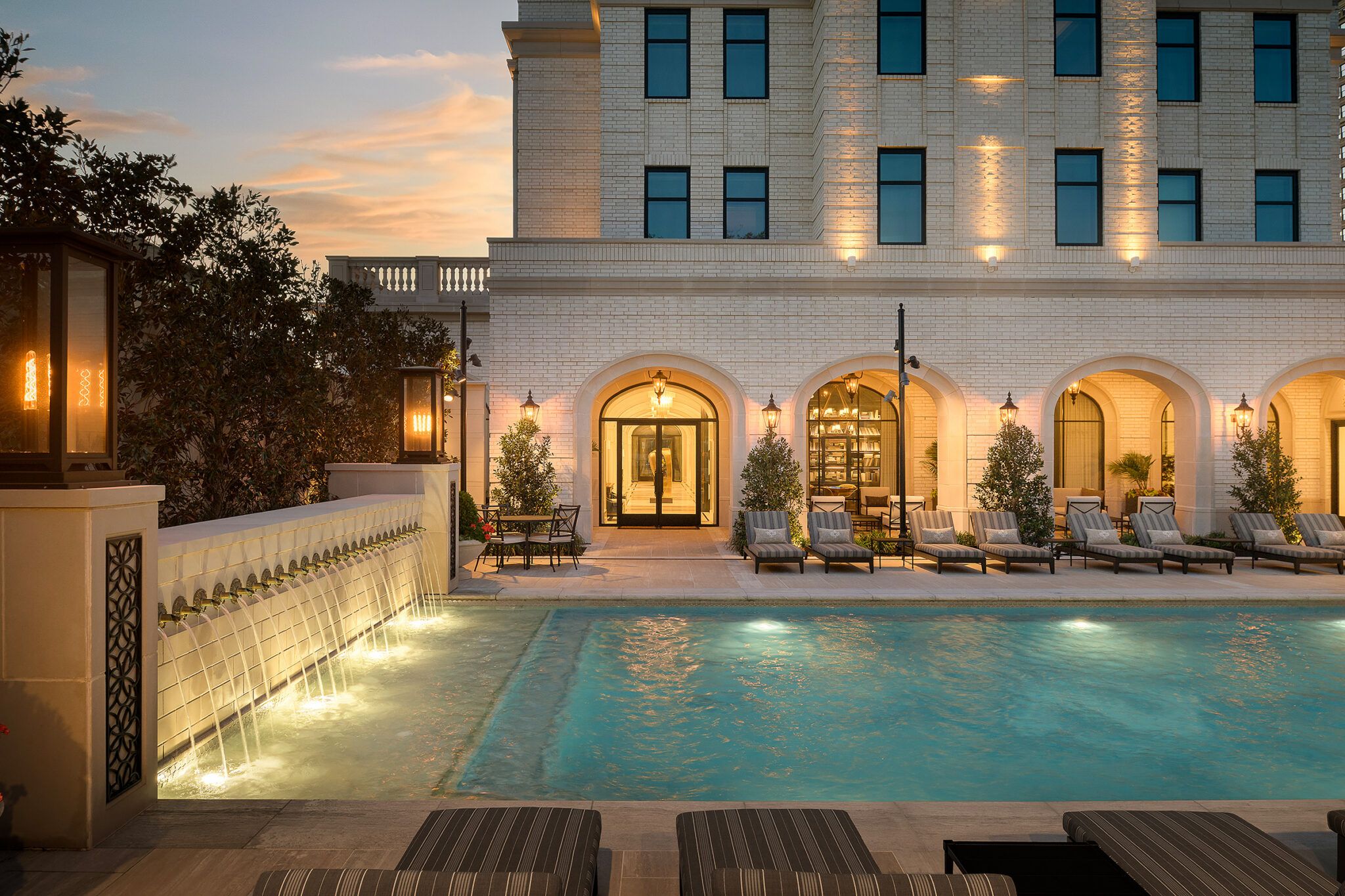 Pool court with sheer-descent fountain wall at dusk
