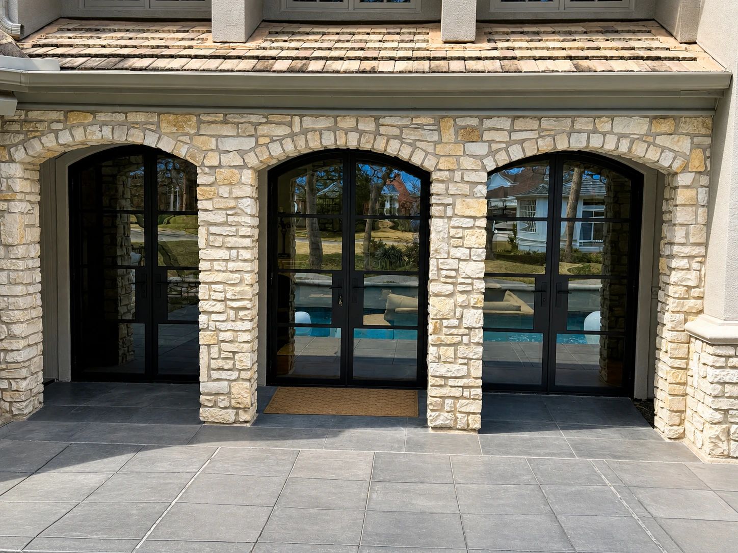 Full exterior elevation of three matching arched black steel double doors set into a pale stone arcade beside a Dallas pool