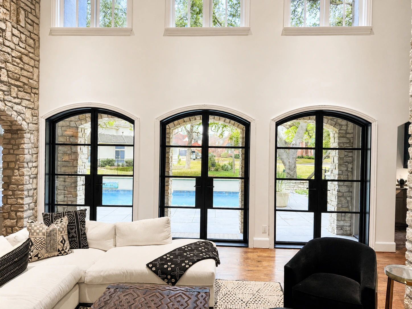 Interior view of three matching arched black steel double doors opening the den to a sunny Dallas pool courtyard