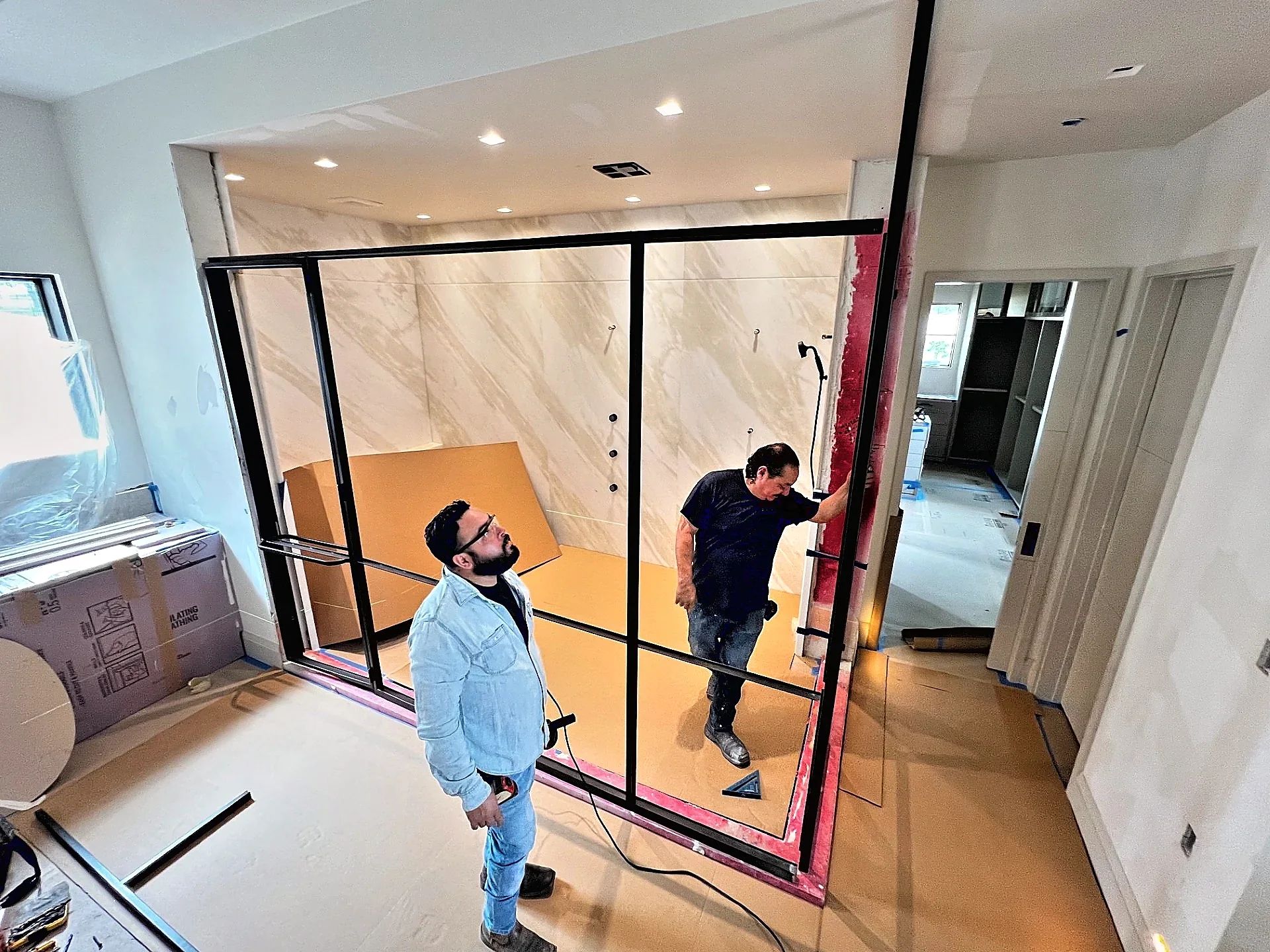 D'Hierro installers setting a full-height espresso steel shower enclosure around a marble wet room in Westlake, Texas