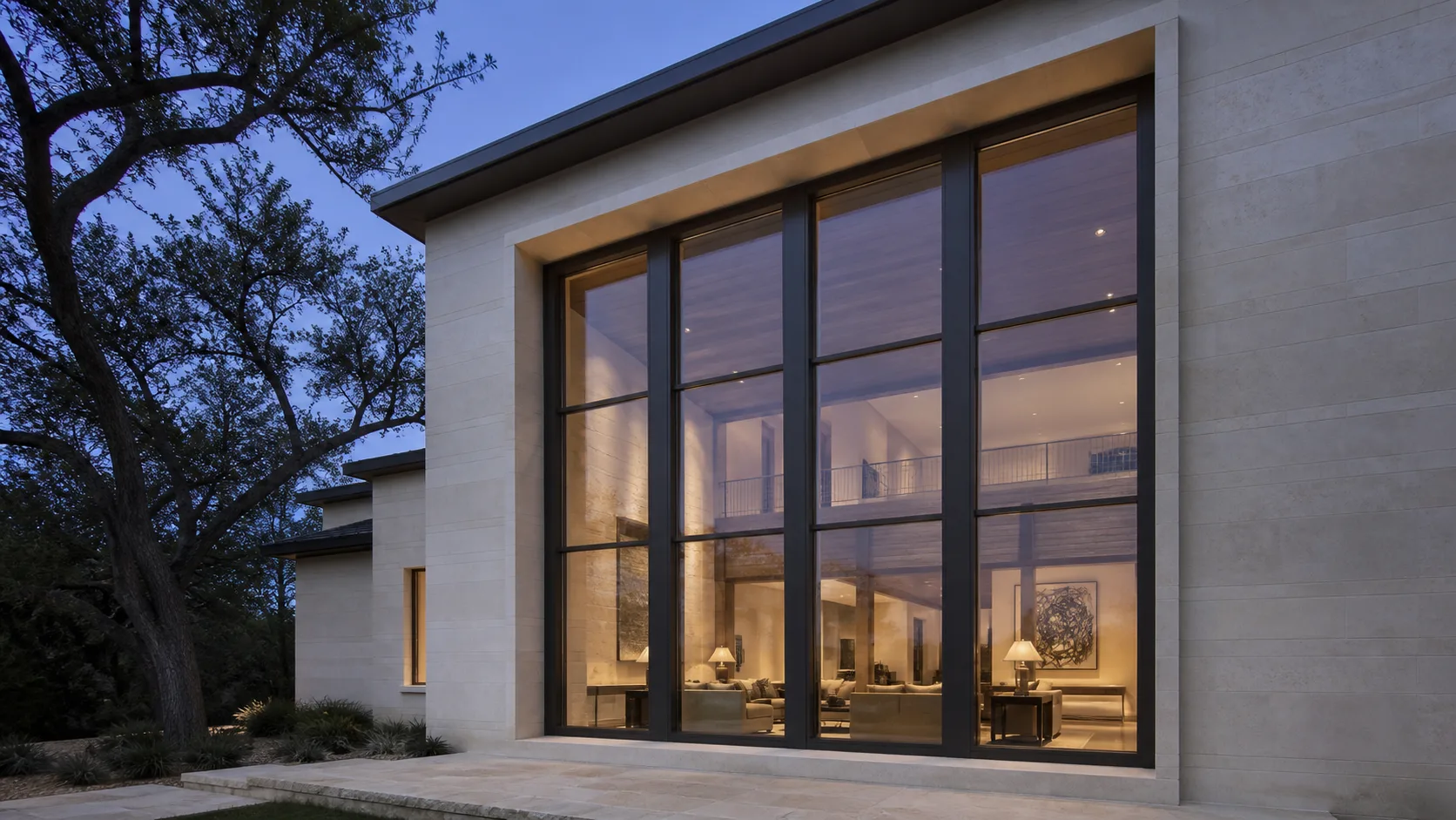 Two-story charcoal steel window wall recessed into a pale limestone facade at blue hour